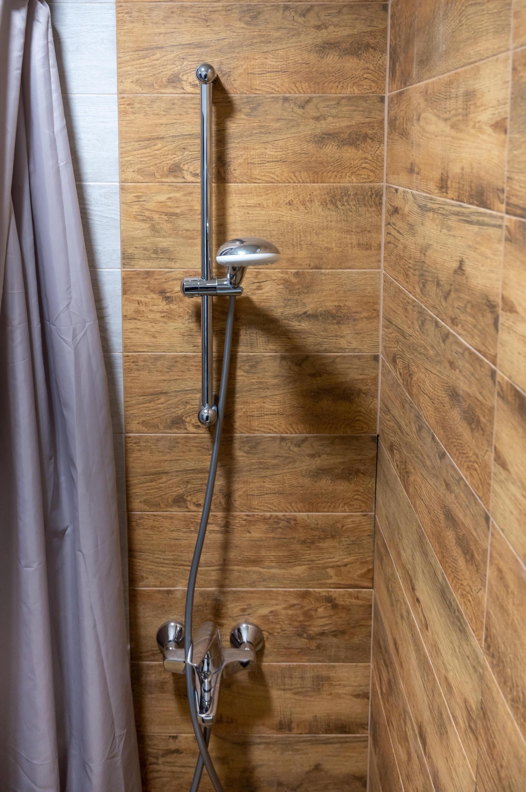 A shower with a chrome hose and wall-mounted controls, adjacent to a wooden panel wall.