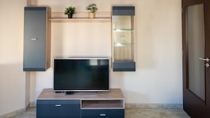 A modern living room with a flat-screen TV on a wooden TV stand, flanked by dark wall-mounted cabinets and a glass shelf unit. - Design Loft in the City Center (Sofia)