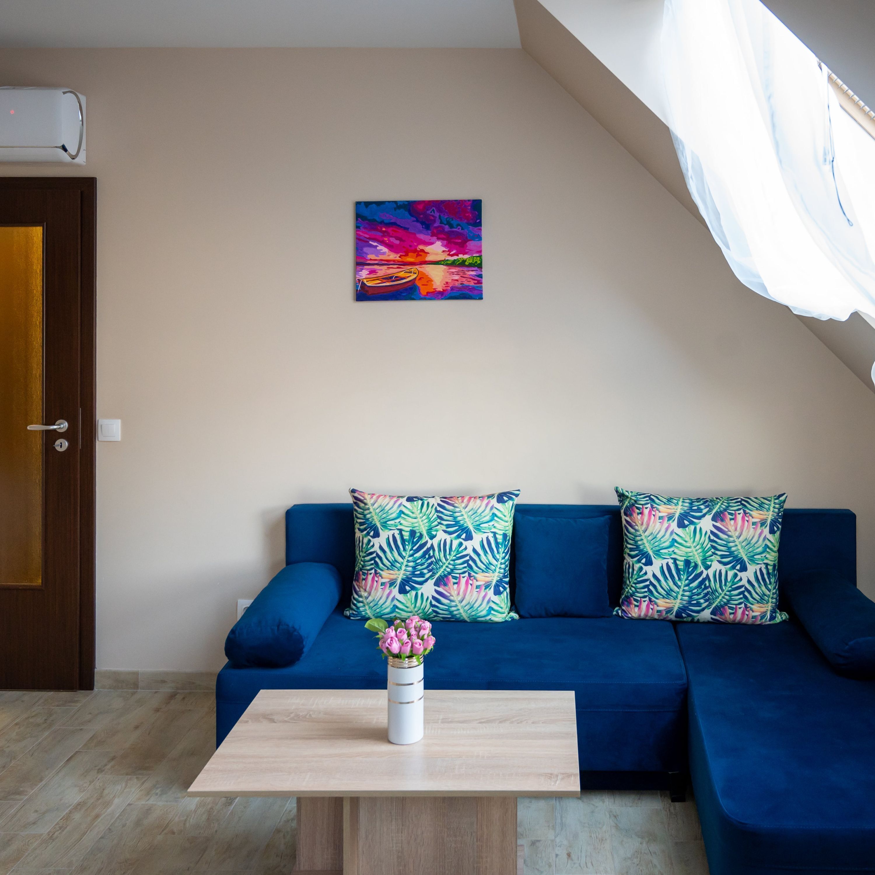A modern living room with a blue sofa, a wooden coffee table, and a colorful painting on the wall.