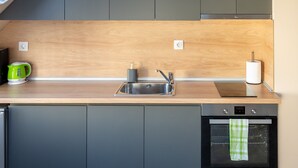 A modern kitchen with grey cabinets, a wooden countertop, a sink, a kettle, and an oven. - Design Loft in the City Center (Sofia)