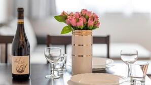 Een eettafel gedekt met een wijnfles, een vaas met roze bloemen en verschillende glazen.