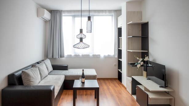 Een moderne woonkamer met een bank, een salontafel, een televisie op een houten dressoir en hanglampen.