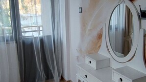 Ein Zimmer mit weißem Schminktisch, einem runden Spiegel und durchsichtigen Vorhängen.