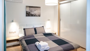 Ein ordentlich bezogenes Bett mit kariertem Überwurf, zwei Nachttischlampen, einem Wandbild und einem Kleiderschrank.