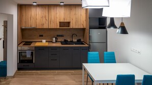 Eine moderne Küche mit Holzschränken, einer weißen Arbeitsplatte, einer Spüle und einem Herd. Ein Esstisch mit blauen Stühlen steht daneben.