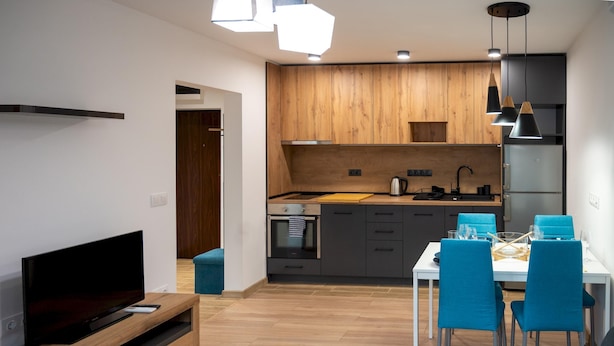 Eine moderne Küche mit Holzausstattung, einem eingebauten Ofen und einem Essbereich mit blauen Stühlen und einem weißen Tisch.