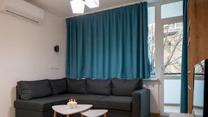 Ein modernes Wohnzimmer mit einem dunkelgrauen Sofa, zwei weißen Beistelltischen und einem Türkisenvorhang.