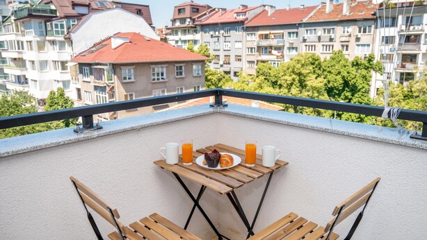 Un balcone con un tavolo apparecchiato per la colazione, con un piatto di cibo, due bicchieri di succo d'arancia e una bottiglia d'acqua.