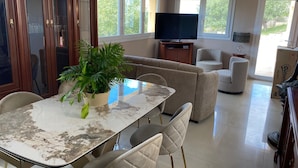 A spacious living room with a large TV, comfortable seating, and a dining area with a marble table. - Appatement Premium 2 Chambres (El Mas Isaac)