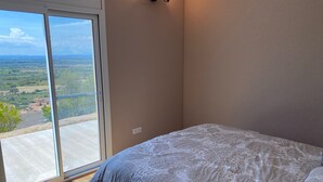 A bedroom with a large sliding glass door leading to a balcony, a bed with patterned bedding, and a wall-mounted light fixture. - Appatement Premium 2 Chambres (El Mas Isaac)