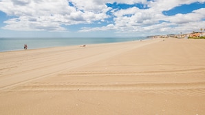 Een breed, zanderig strand met een heldere lucht en een rustige zee.