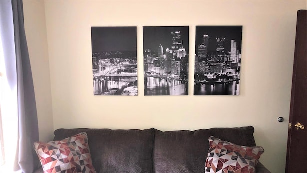A grey sofa with patterned cushions, a cityscape wall art, and a door to the right.