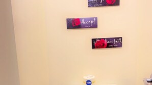 A small bathroom with a toilet, a trash bin, a toilet paper holder, and a plunger. There are three motivational signs on the wall.