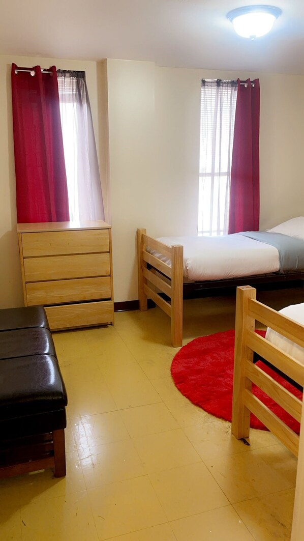 A small, well-lit room with two beds, a wooden dresser, and a red rug. - 2 Bedroom Downtown Apt Friends Families Ideal (Pittsburgh)