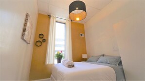 Una camera d'albergo con un letto, una finestra con tende, una pianta in vaso e un lampadario a parete.