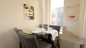 Zona pranzo con tavolo in vetro, quattro sedie e una finestra vista edifici.