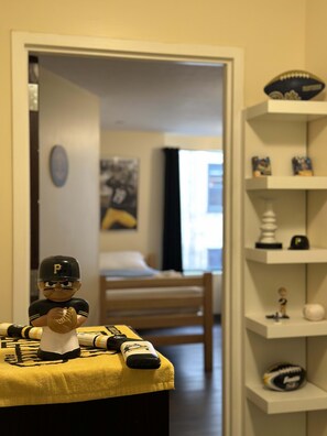 Una habitación con cama, una silla y una estantería con recuerdos deportivos.