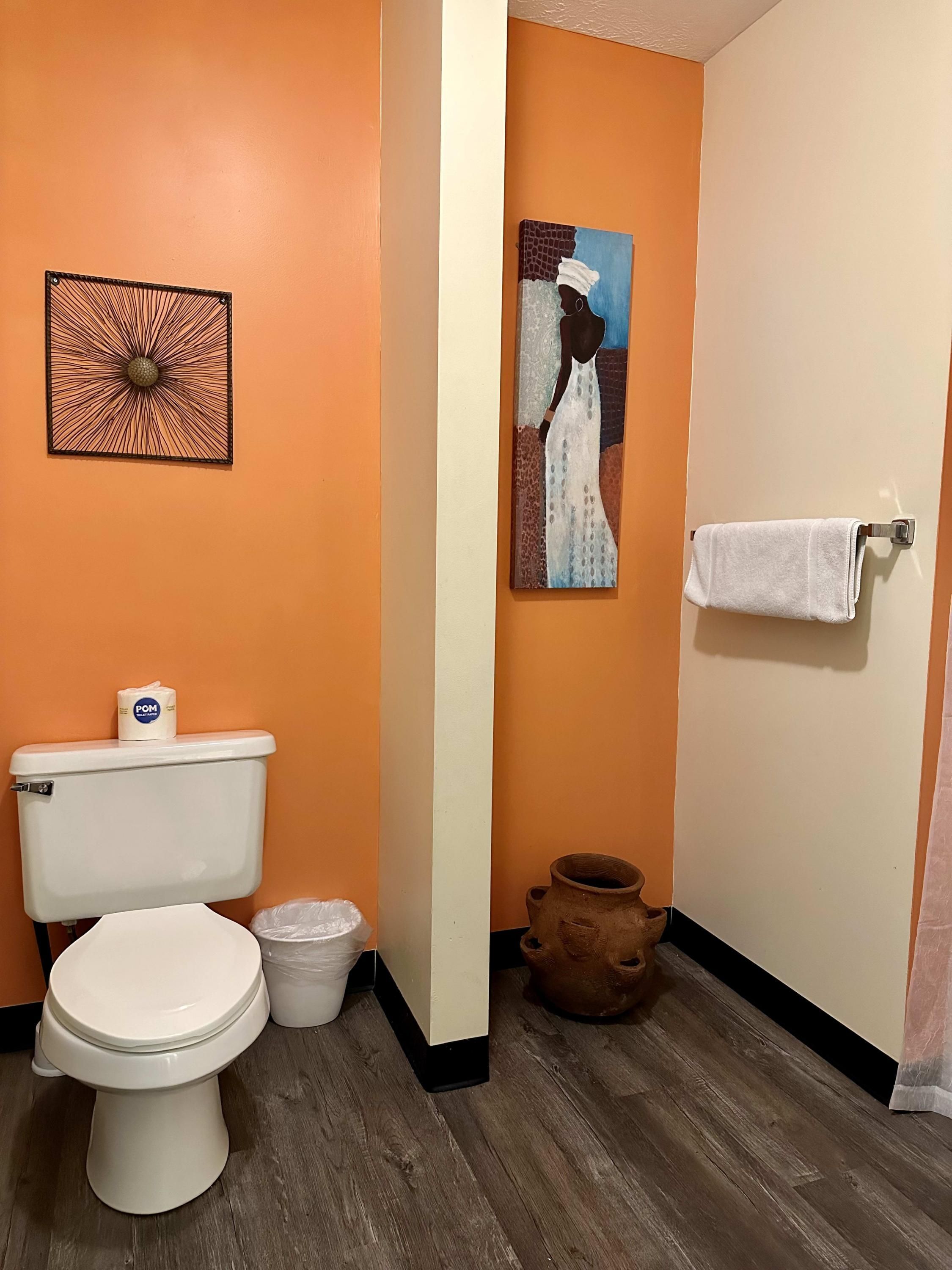 Ein Badezimmer mit oranger Wand, Toilette, Waschbecken, Handtuchhalter und einem Gemälde.