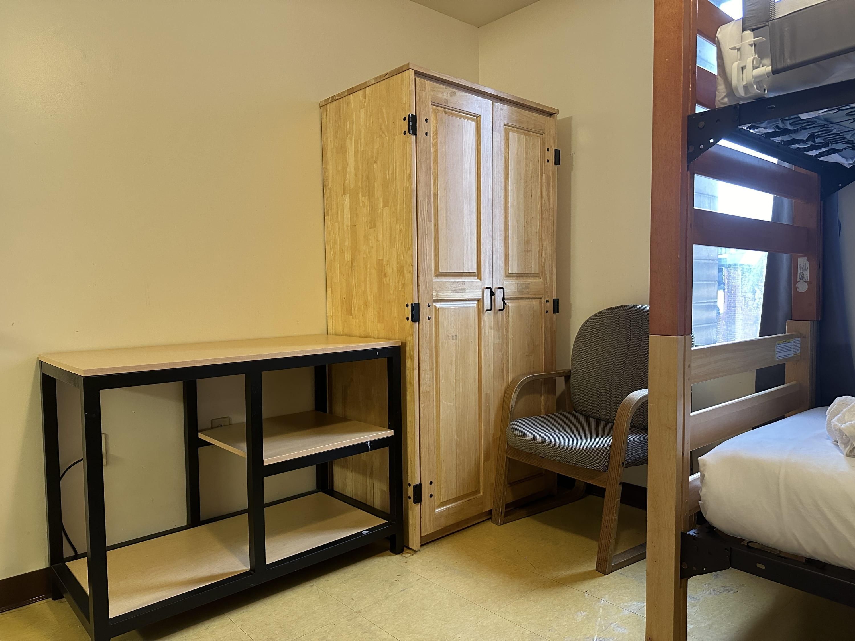 Ein Zimmer mit einem Etagenbett, einem Holzschrank, einem Stuhl und einem kleinen Tisch.