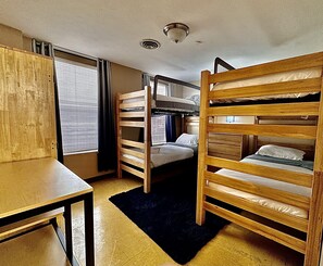 A dorm-style room with bunk beds, a desk, and a window with blinds. - 7 Beds Explore Downtown Pittsburgh Large Groups (Pittsburgh)
