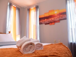 Une chambre d’hôtel avec un lit, des serviettes roulées et un tableau représentant un coucher de soleil accroché au mur.