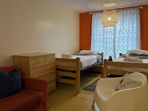 Une chambre de dortoir avec deux lits superposés en bois, une commode en bois, un canapé rouge et un fauteuil blanc.