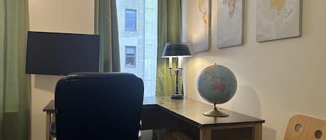 A room with a desk, a chair, a globe, a lamp, a window with curtains, and a wall map.