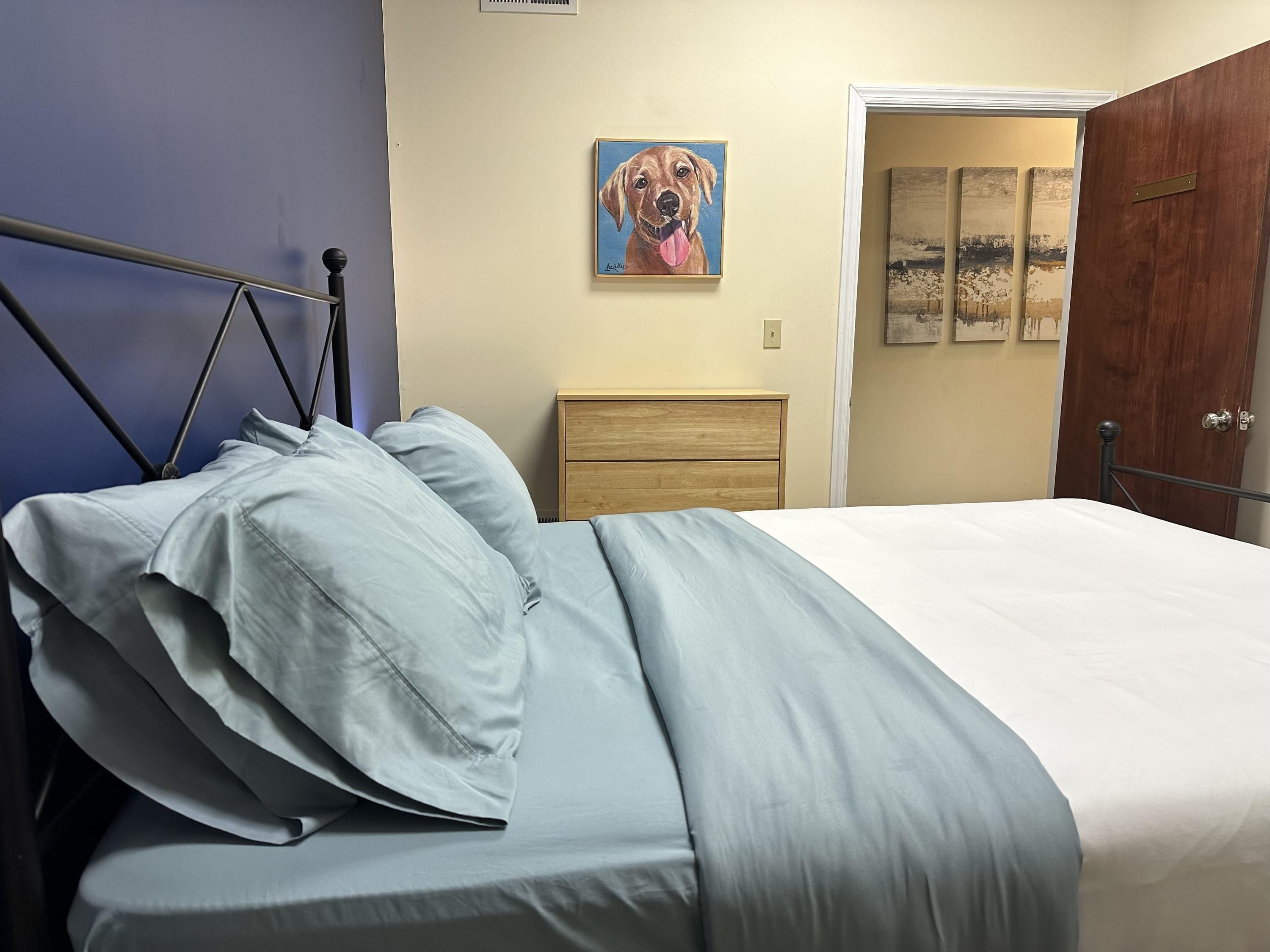 Een slaapkamer met een bed, nachtkastje, houten dressoir en een deur.