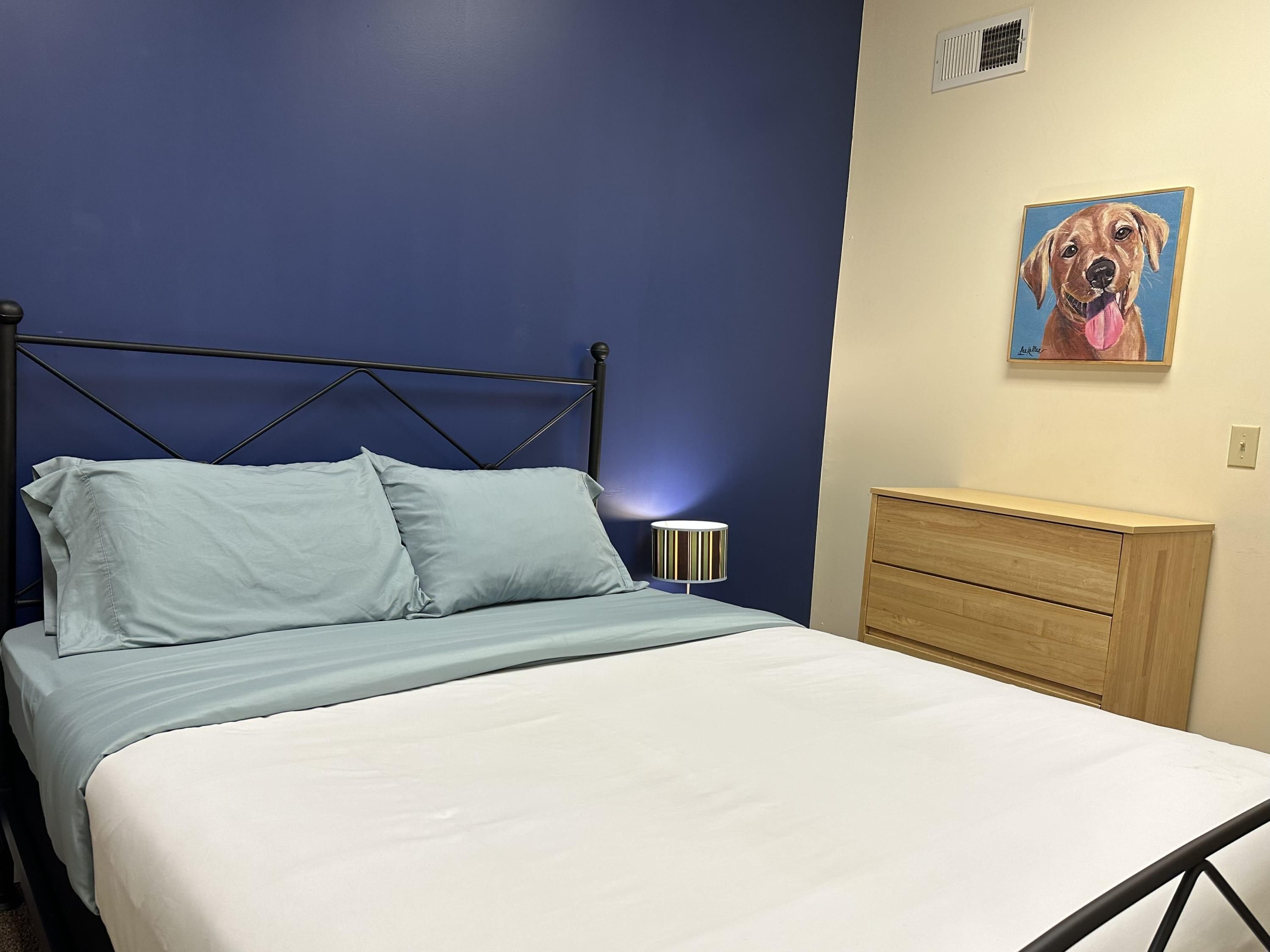 Un lit avec une tête de lit bleue, une lampe de chevet et une commode en bois.