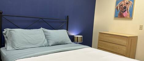A bed with a blue headboard, a bedside lamp, and a wooden dresser.
