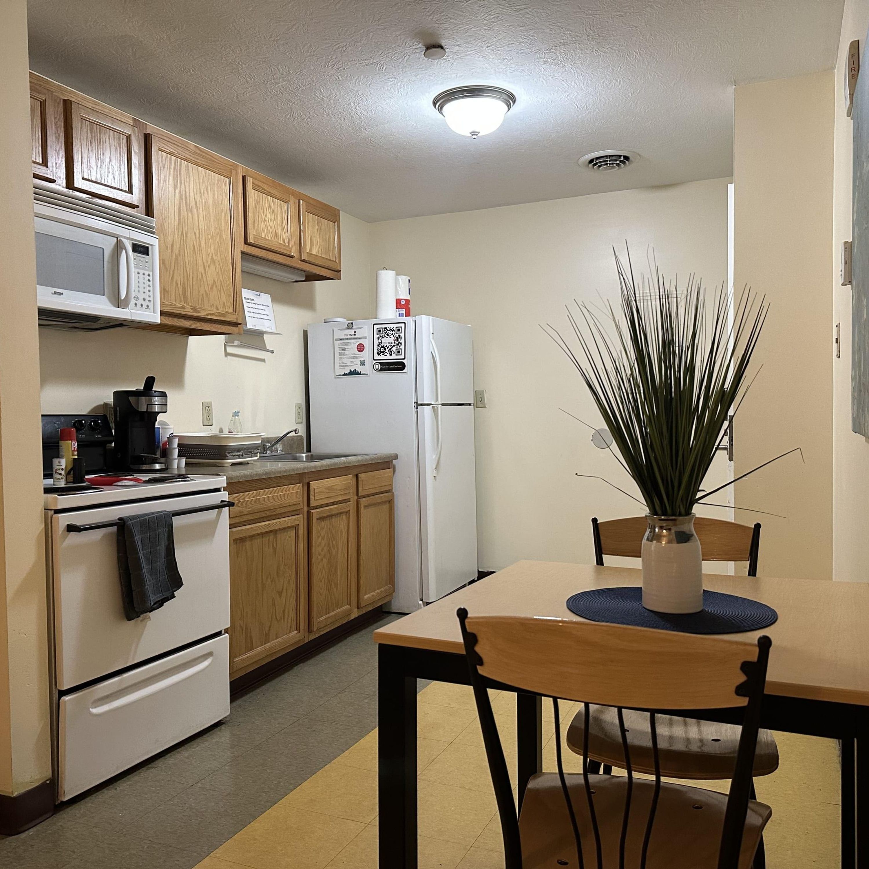 A compact kitchen with wooden cabinets, a microwave, a refrigerator, and a dining area with a table and chairs.