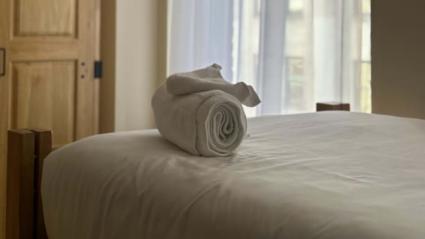 Siisti hotellihuone, jossa on huolitellusti pedattu sänky, puinen vaatekaappi ja ikkuna, jossa on ohuet verhot.