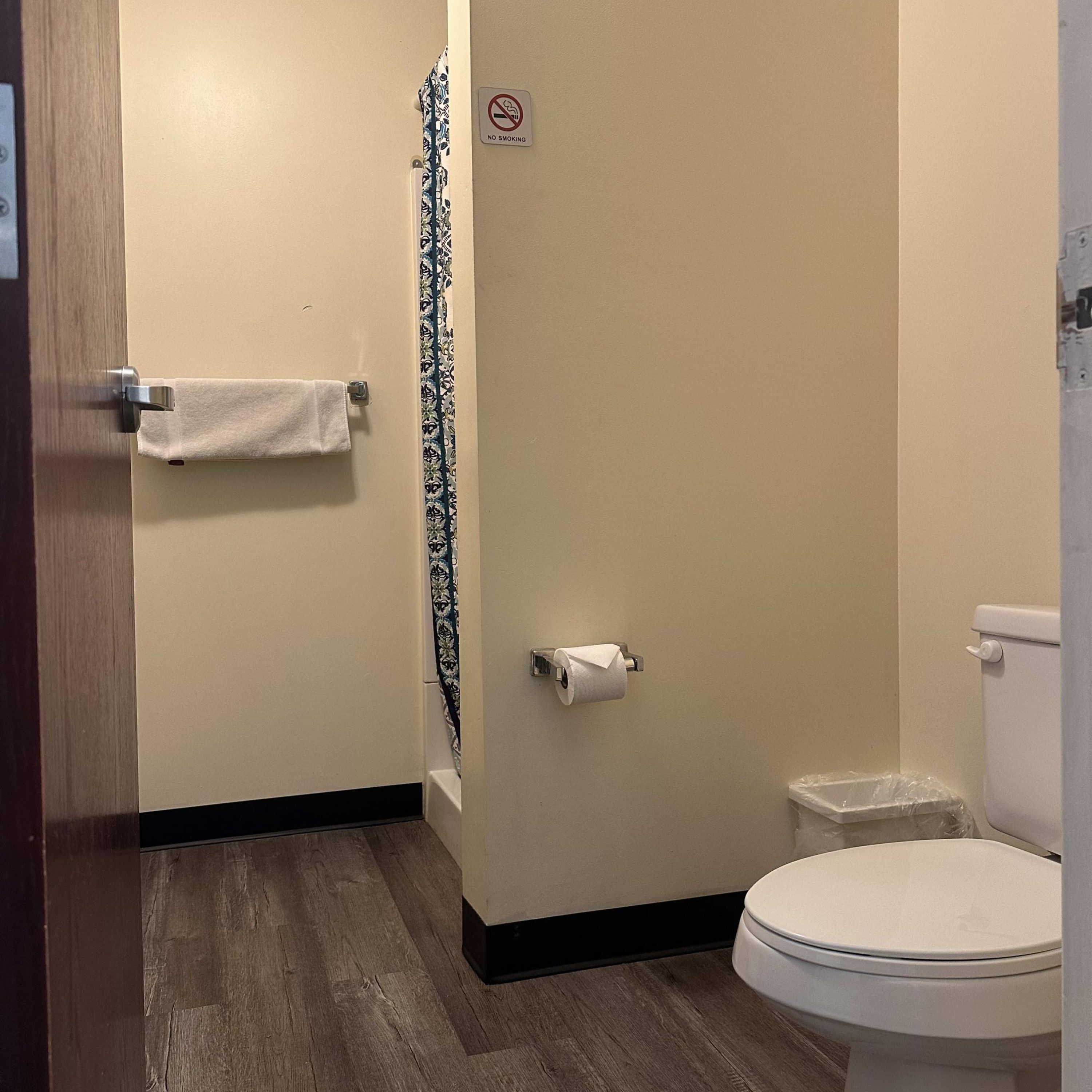 A bathroom with a toilet, a towel rack, a toilet paper holder, and a no smoking sign.