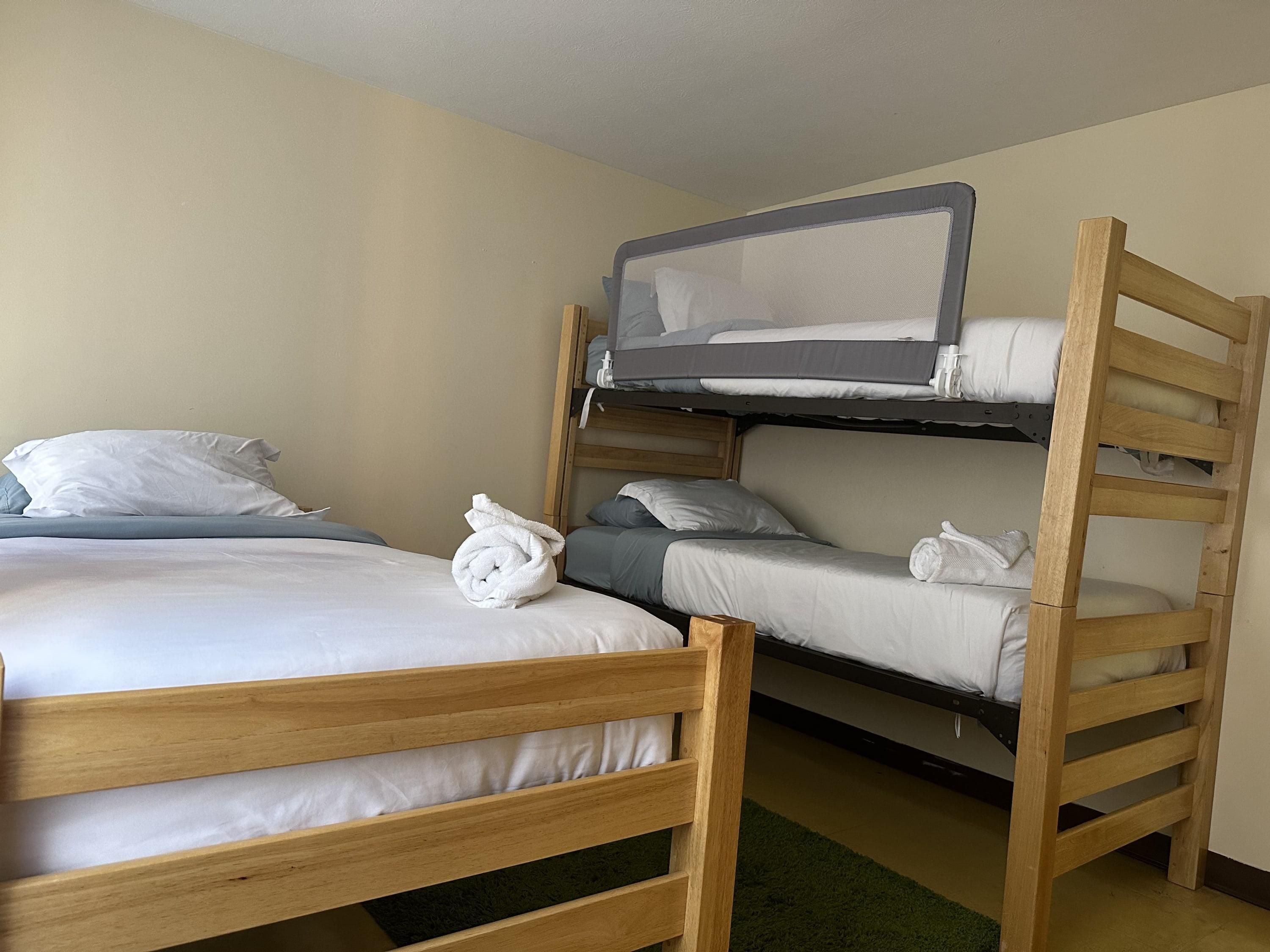 A bunk bed room with a wooden ladder, a single bed with white bedding, and a bunk bed with grey bedding.