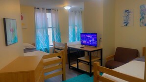 A compact hotel room with two single beds, a desk with a chair, a television, and a window with curtains.
