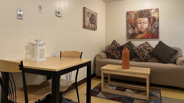 A living room with a dining table, chairs, a sofa, and a coffee table. There are wall-mounted smoke detectors and a painting of a Buddha.