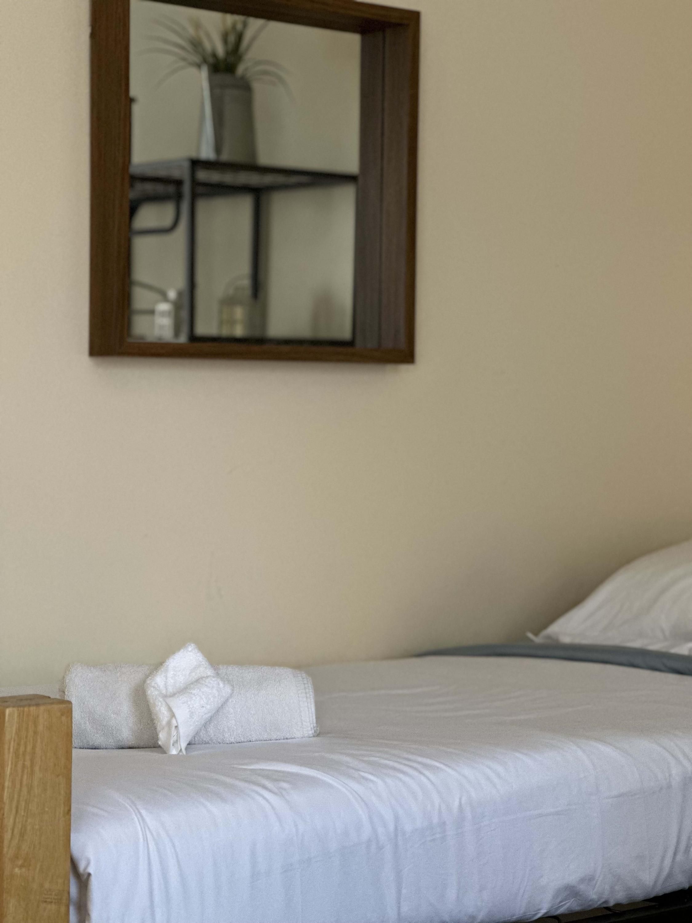 A neatly made bed with white linens and pillows, a wooden headboard, and a mirror on the wall.