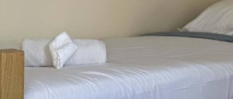 A neatly made bed with white linens and pillows, a wooden headboard, and a mirror on the wall.