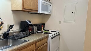 A compact kitchen with wooden cabinets, a white stove, a microwave, and a dish rack. - 2 Bedroom Downtown Apt Walkable Safe Clean (Pittsburgh)