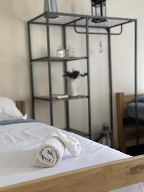 A neatly made bed with a rolled white towel on the side, a wooden headboard, and a black metal shelf unit with decorative items in the background. - 2 Bedroom Downtown Apt Walkable Safe Clean (Pittsburgh)