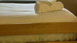 Ein ordentlich bezogenes Bett mit einem zusammengerollten Handtuch, einem Kopfkissen und einem hölzernen Kopfteil.