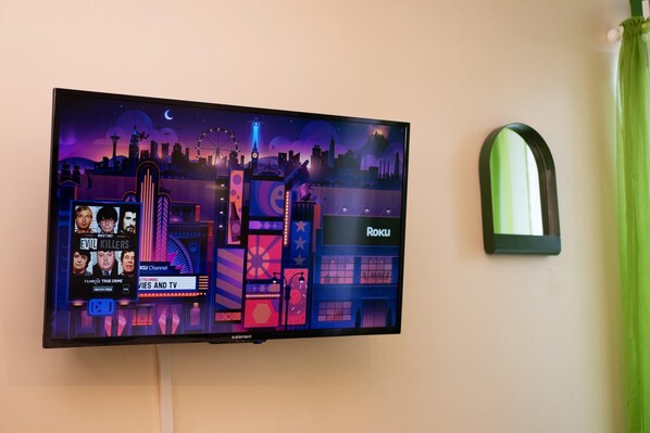 A flat-screen TV mounted on a wall displaying a cityscape with a neon sign reading "Roku." - Downtown Apt Walk to all Stadiums Conv Center (Pittsburgh)