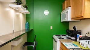 A compact kitchen with a green wall, white cabinets, a microwave, a stove, and a small dining area with a chair. - Downtown Apt Walk to all Stadiums Conv Center (Pittsburgh)