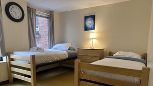 A room with two wooden bunk beds, a wall clock, a window with curtains, a nightstand with a lamp, and a painting on the wall. - 2 Bedroom 2 Bath City Views (Pittsburgh)