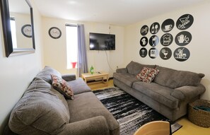 A living room with a grey sofa, a television, and a wall decorated with drink and food icons. - 2 Bedroom 2 Bath City Views (Pittsburgh)