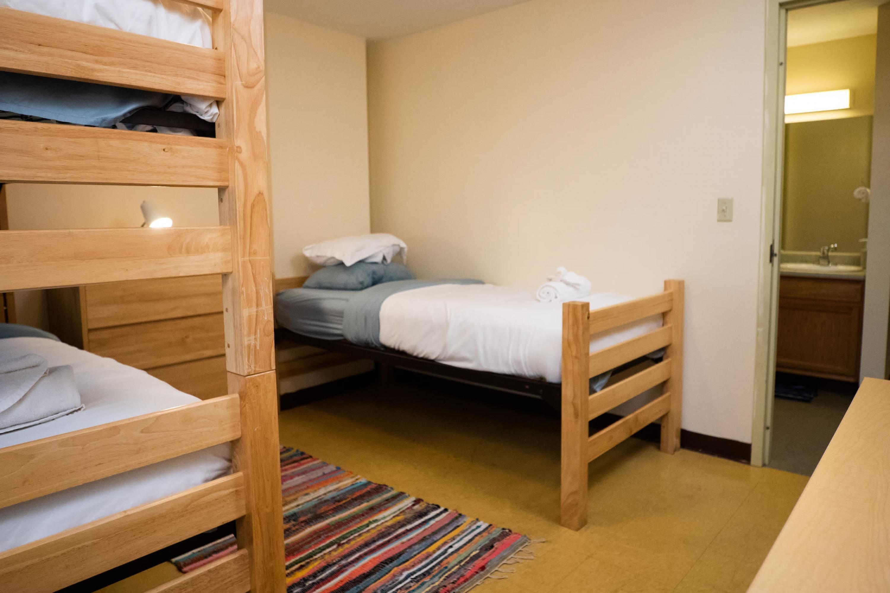 A small, cozy room with two bunk beds, a single bed, a wooden door, and a small bathroom visible through an open door.