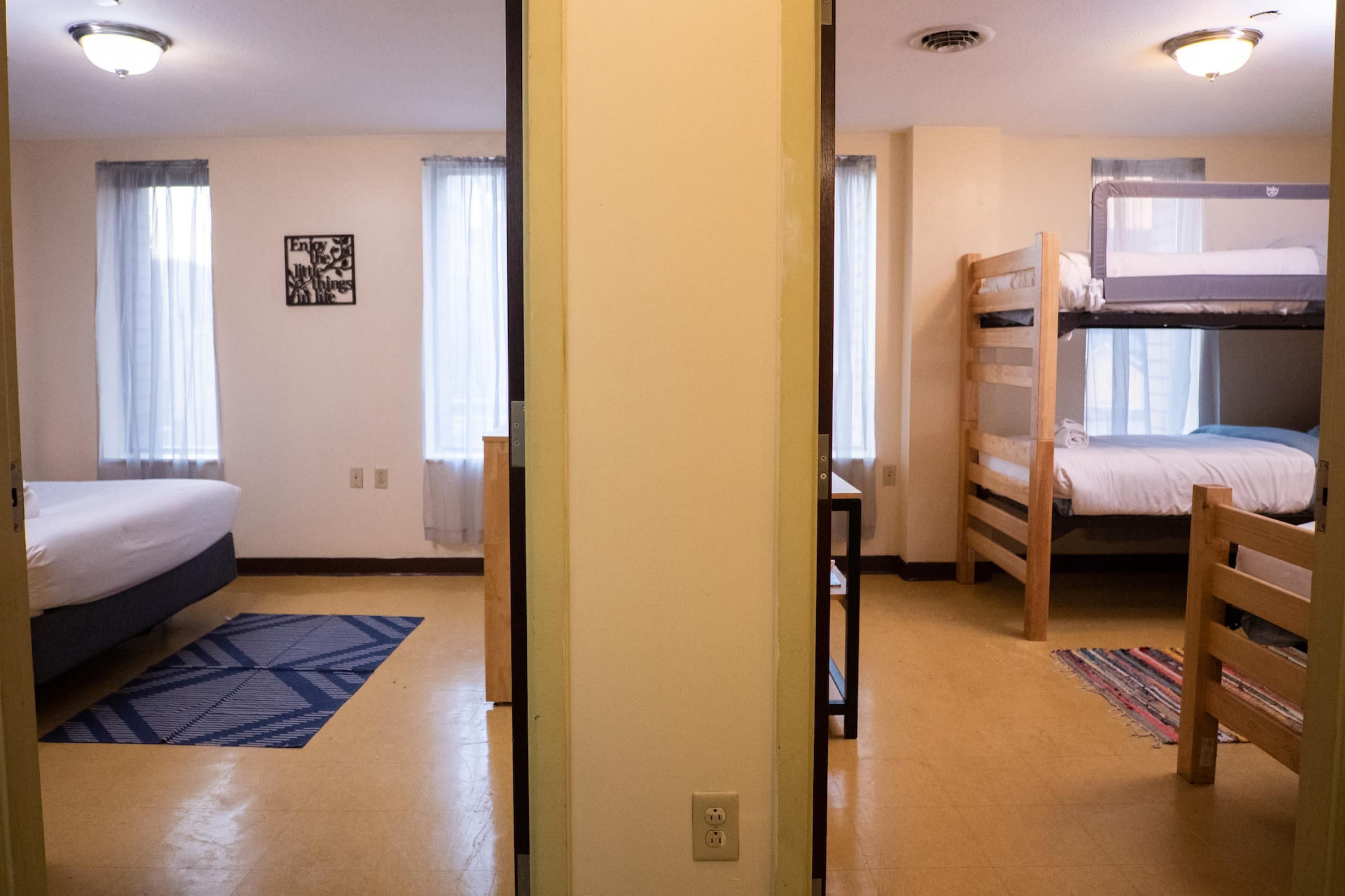 A dormitory room with bunk beds, a desk, and a window with curtains.