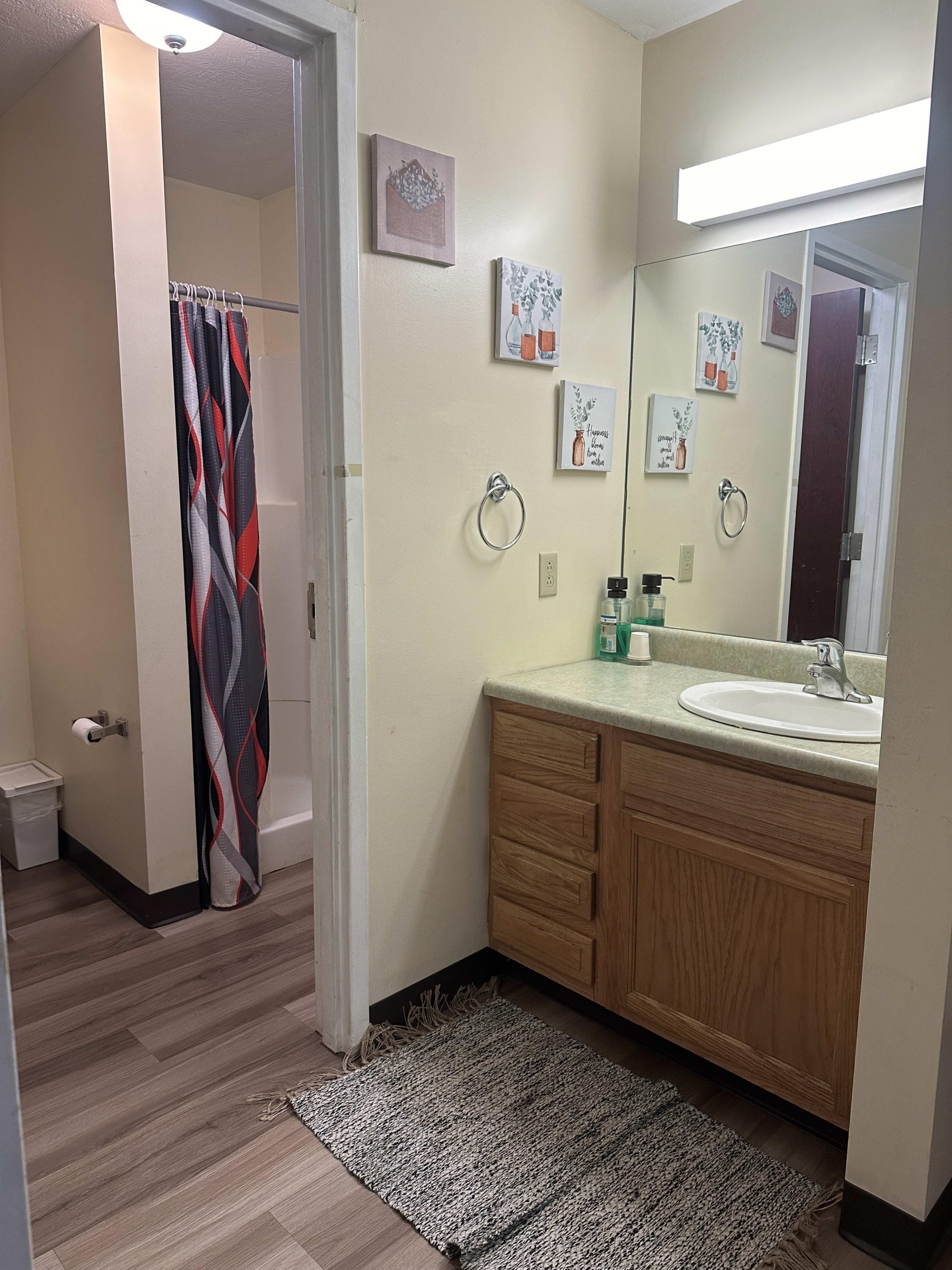 A bathroom with a wooden vanity, a sink, a mirror, and a shower curtain.