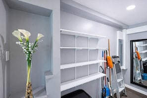 A room with a white shelf unit, a vase with flowers, and cleaning tools.