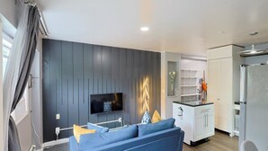 A modern living room with a flat-screen TV, a blue sofa, and a kitchen area with white cabinets and a refrigerator. - Stylish and Pet-Friendly Apartment in Beacon (Beacon)